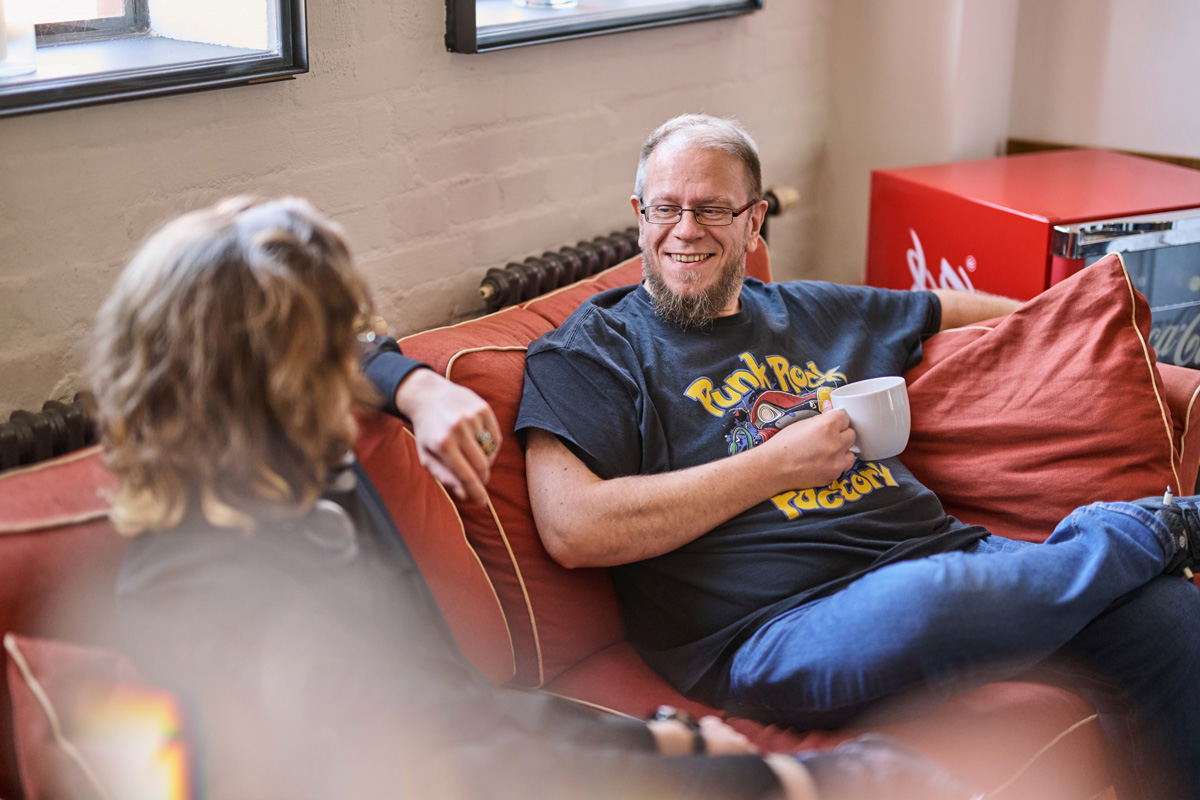 Ein soft-park-Mitarbeiter sitzt entspannt mit einer Kaffeetasse auf einem Sofa und unterhält sich mit einem Kollegen